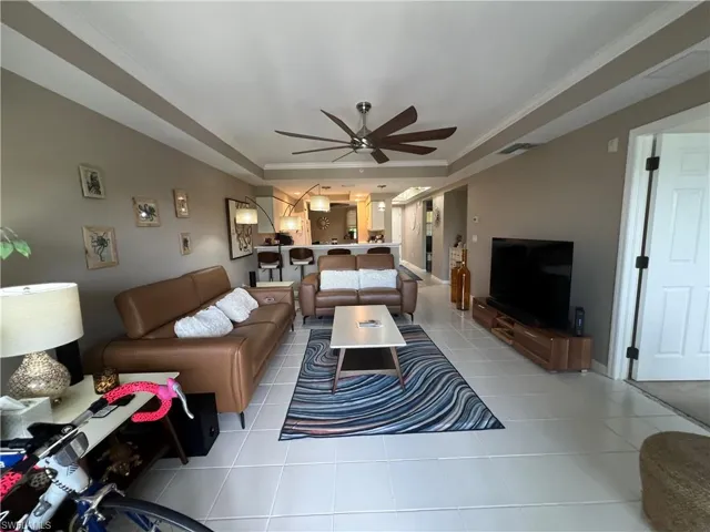Living area featuring ornamental molding, light tile patterned floors, a ceiling fan, and a raised ceiling