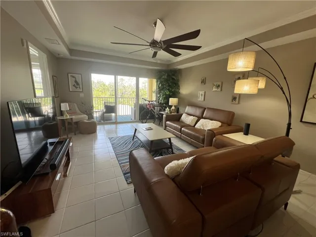 Tiled living area featuring a tray ceiling, ornamental molding, and ceiling fan