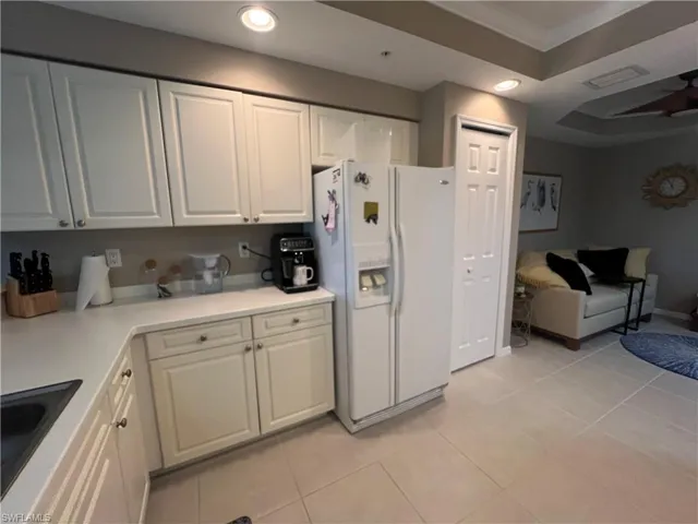 Kitchen featuring recessed lighting, white refrigerator with ice dispenser, light tile patterned floors, white cabinets, and light countertops