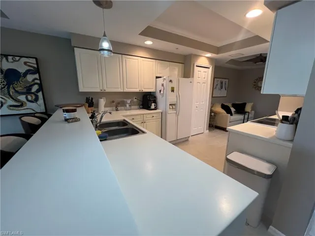 Kitchen with white fridge with ice dispenser, recessed lighting, a raised ceiling, white cabinetry, and pendant lighting