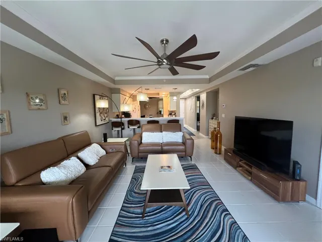 Living room featuring crown molding, a tray ceiling, a ceiling fan, and tile patterned floors
