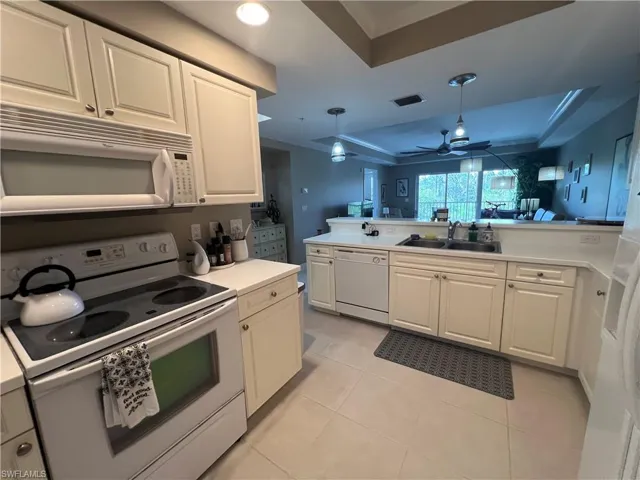 Kitchen featuring a raised ceiling, white appliances, white cabinets, light countertops, and recessed lighting