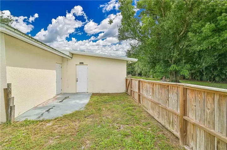 Exterior property side featuring a wooden privacy fence, stucco siding, and a concrete patio area