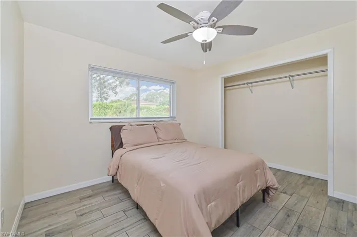 Bedroom featuring wood-finish tile flooring, a window with horizontal blinds, an open closet with a hanging rod, and a ceiling fan with integrated lighting