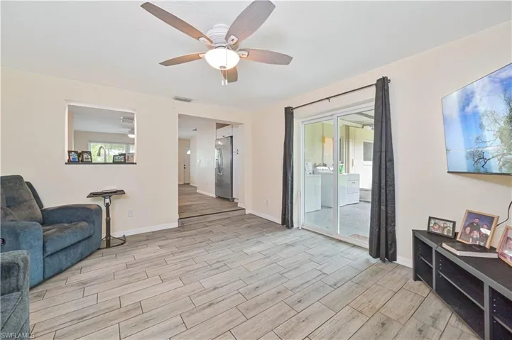 Spacious living area featuring wood-look tile flooring, a ceiling fan with light fixture, and a pass-through window