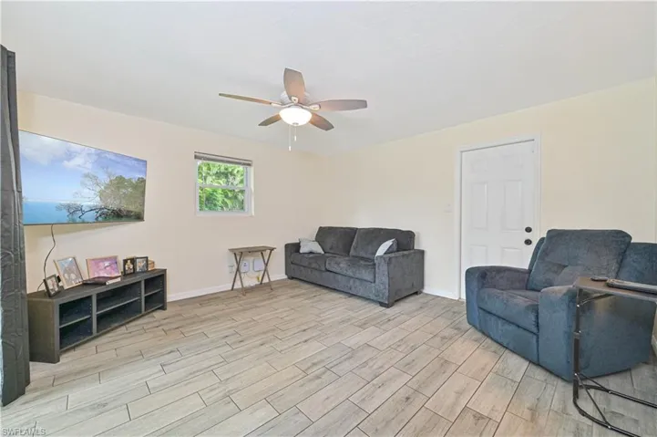 Spacious living area featuring wood-finish tile flooring, a ceiling fan with integrated lighting, and a white paneled door