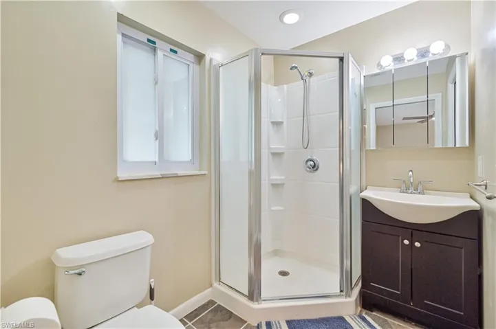 Bathroom featuring a corner shower enclosure, a single-sink vanity with dark wood cabinetry, a toilet, a window with frosted glass, and recessed lighting