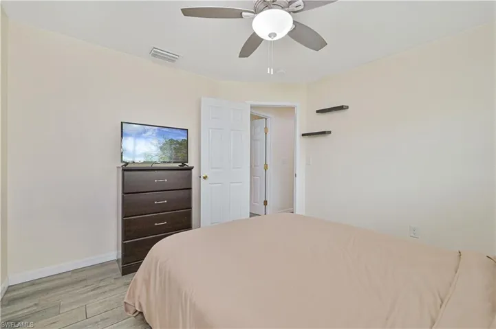Bedroom featuring light-toned walls, wood-finish flooring, a ceiling fan with integrated lighting, and a white paneled door