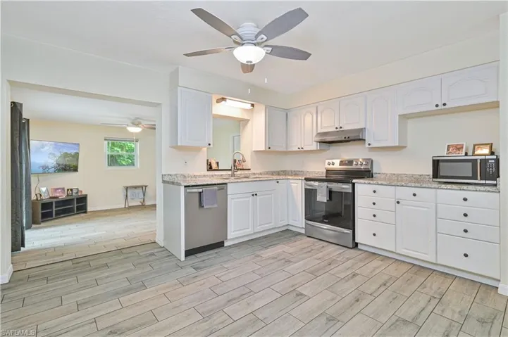 Kitchen featuring white cabinetry, granite-finish countertops, stainless steel appliances, and wood-look tile flooring