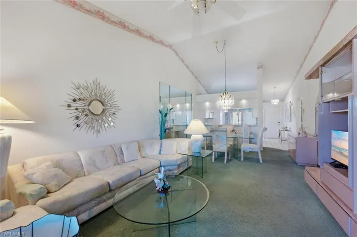Living room featuring ceiling fan, carpet flooring, vaulted ceiling, and a chandelier