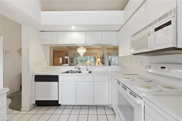 Kitchen with white appliances, suspended lighting, white cabinets, and light countertops