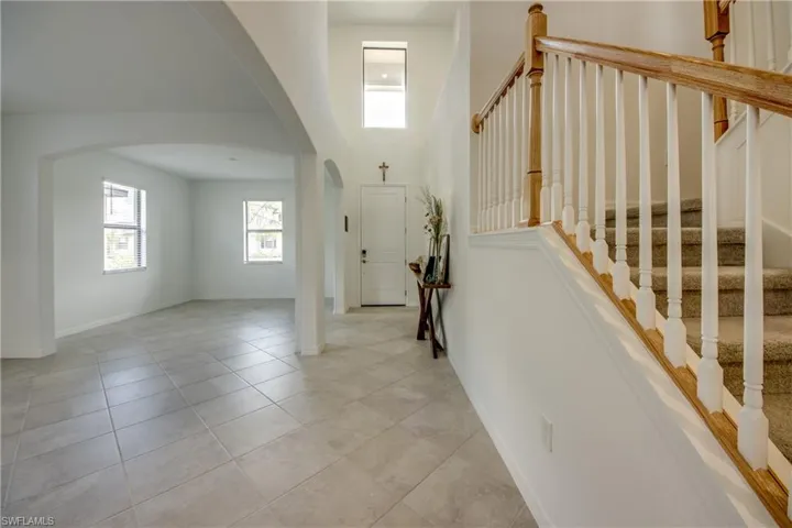 Foyer entrance with healthy amount of natural light, arched walkways, light tile patterned floors, a high ceiling, and stairs
