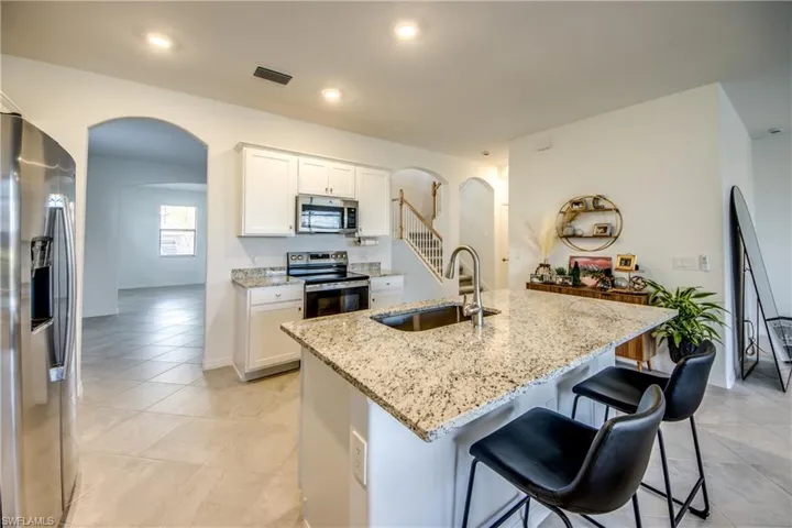 Kitchen with arched walkways, stainless steel appliances, light stone counters, white cabinets, and light tile patterned floors