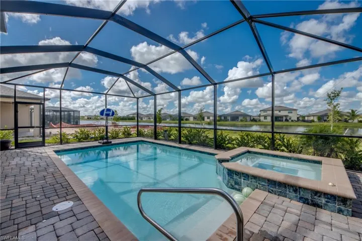 View of pool featuring a sunroom, a residential view, glass enclosure, a pool with connected hot tub, and a water view