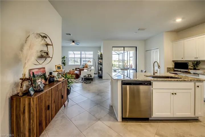 Kitchen with white cabinets, dishwasher, light stone countertops, open floor plan, and light tile patterned floors