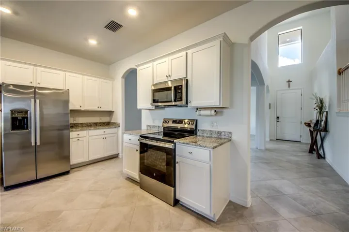 Kitchen with stainless steel appliances, arched walkways, white cabinetry, light stone counters, and recessed lighting