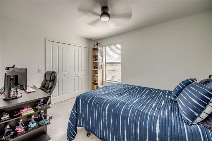 Bedroom featuring light colored carpet, an office area, a closet, and ceiling fan