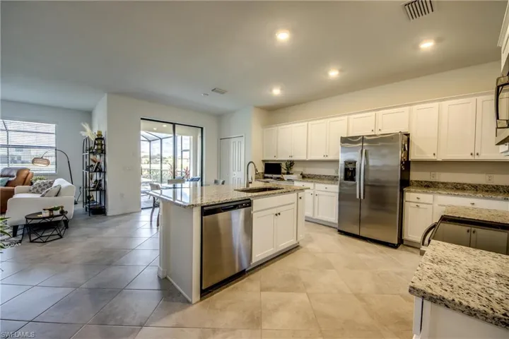 Kitchen featuring stainless steel appliances, light stone counters, white cabinetry, a kitchen island with sink, and recessed lighting