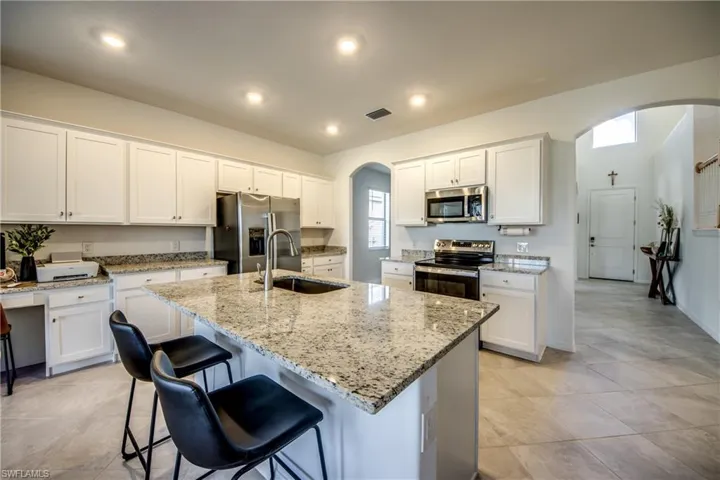 Kitchen featuring arched walkways, stainless steel appliances, white cabinetry, light stone countertops, and a center island with sink