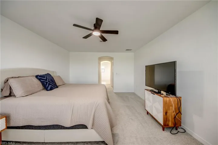Bedroom with arched walkways, a ceiling fan, and light carpet