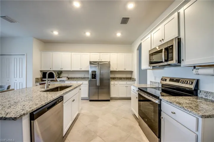 Kitchen featuring appliances with stainless steel finishes, white cabinetry, light stone countertops, and recessed lighting