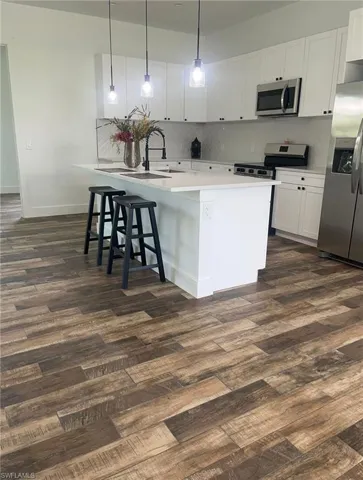 Kitchen featuring stainless steel appliances, pendant lighting, a kitchen breakfast bar, white cabinets, and dark wood-style floors