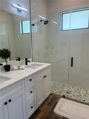 Full bathroom with a shower stall, double vanity, and dark wood-type flooring
