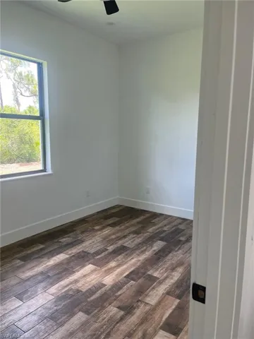 Unfurnished room featuring dark wood-style flooring and ceiling fan