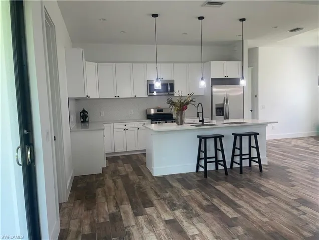 Kitchen with white cabinetry, hanging light fixtures, appliances with stainless steel finishes, and dark wood-type flooring