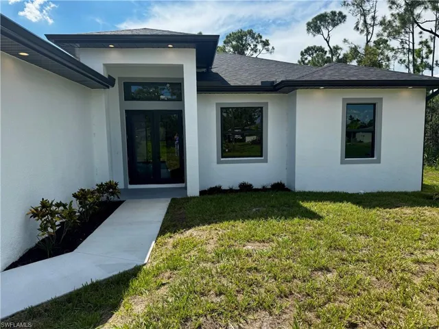 Doorway to property with a yard, stucco siding, french doors, and a shingled roof