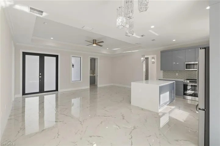 Kitchen featuring appliances with stainless steel finishes, a tray ceiling, crown molding, gray cabinets, and a kitchen island