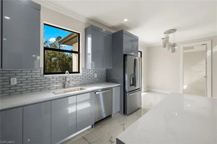 Kitchen featuring light stone countertops, appliances with stainless steel finishes, sink, gray cabinets, and hanging light fixtures