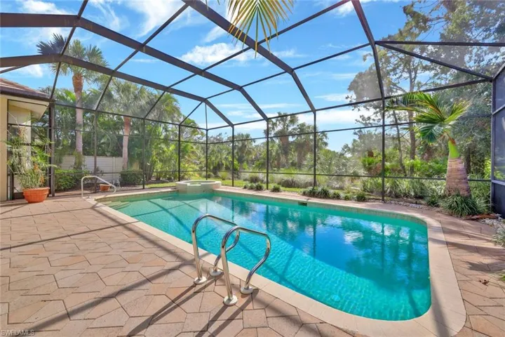View of pool with glass enclosure, a patio area, and an in ground hot tub
