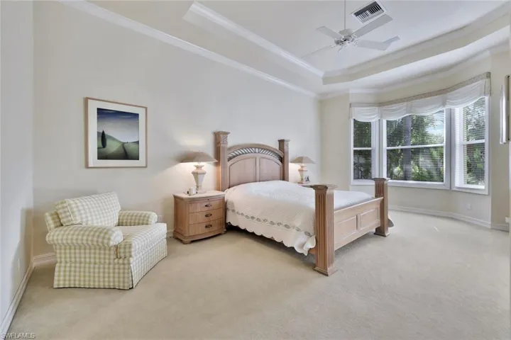 Carpeted bedroom featuring ceiling fan, a raised ceiling, and crown molding