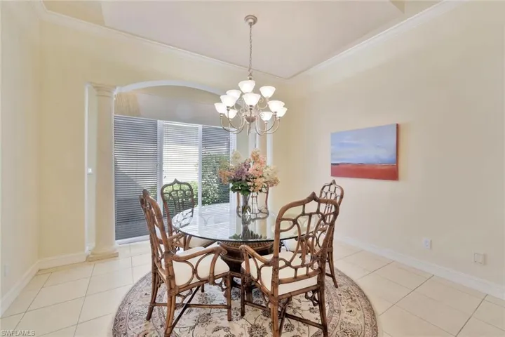 Tiled dining space with decorative columns, an inviting chandelier, and ornamental molding