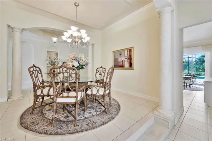 Dining space featuring ornate columns, light tile patterned flooring, ornamental molding, and an inviting chandelier