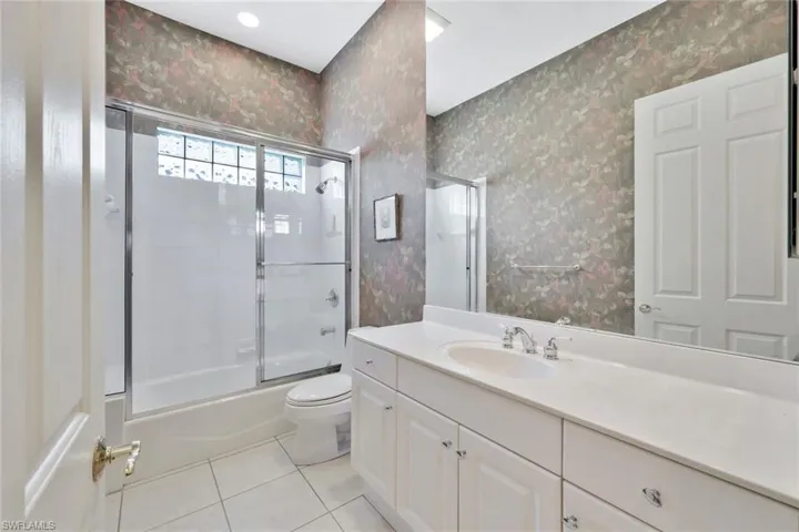 Full bathroom with tile patterned flooring, vanity, toilet, and enclosed tub / shower combo