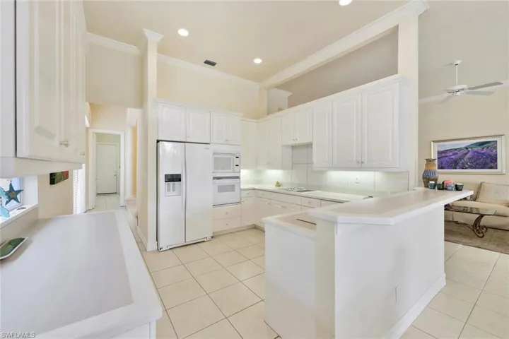Kitchen with white appliances, a high ceiling, white cabinets, light tile patterned floors, and kitchen peninsula