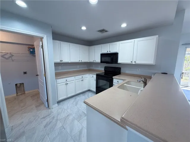 Kitchen with white cabinetry, black appliances, recessed lighting, a peninsula, and light countertops