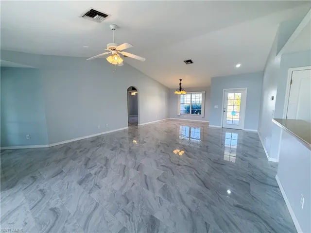 Unfurnished living room with arched walkways, light marble finish flooring, a ceiling fan, and vaulted ceiling