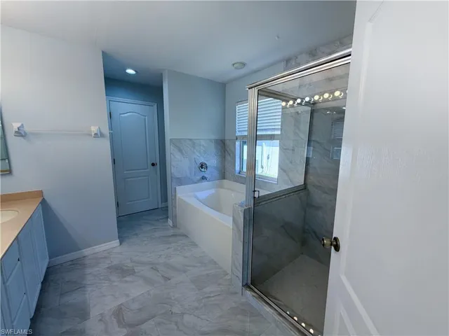 Full bath featuring vanity, a garden tub, a marble finish shower, and light marble finish floors