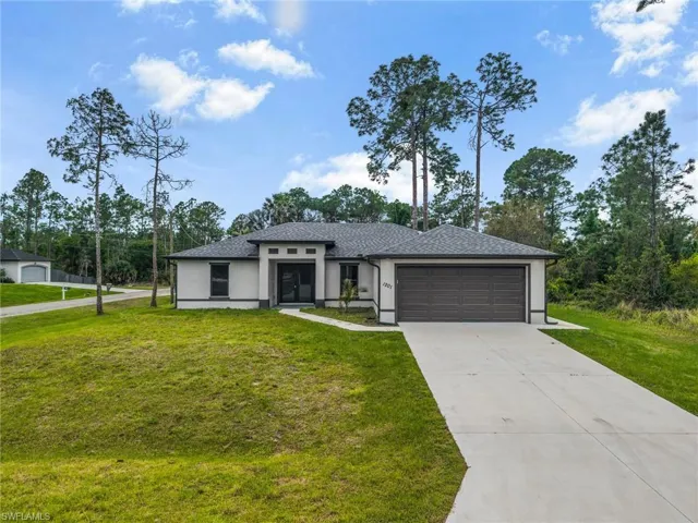 Prairie-style house featuring a front lawn, stucco siding, driveway, a garage, and view of scattered trees