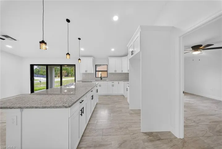 Kitchen featuring a large island, white cabinetry, backsplash, ceiling fan, and light stone counters