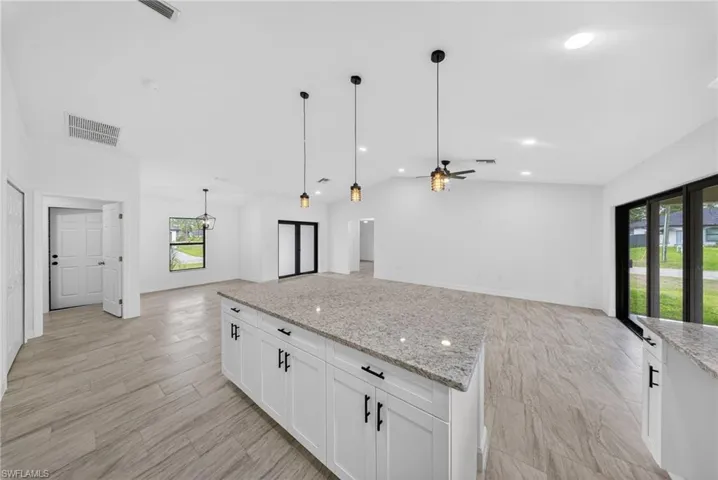 Kitchen with open floor plan, white cabinetry, light stone countertops, a kitchen island, and lofted ceiling