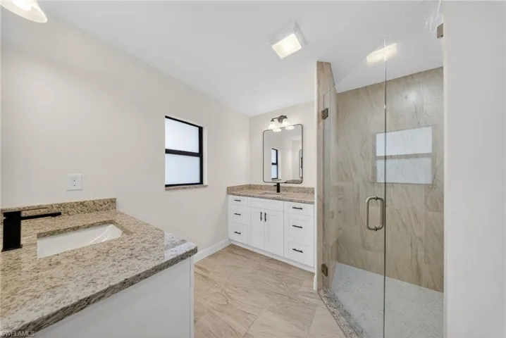 Full bathroom with two vanities, a marble finish shower, and light marble finish floors