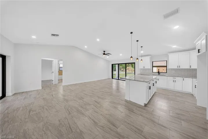 Kitchen featuring open floor plan, decorative backsplash, white cabinets, a ceiling fan, and a kitchen island