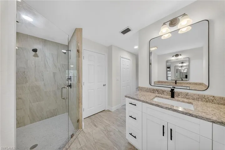 Full bath featuring vanity, a stall shower, and light marble finish floors
