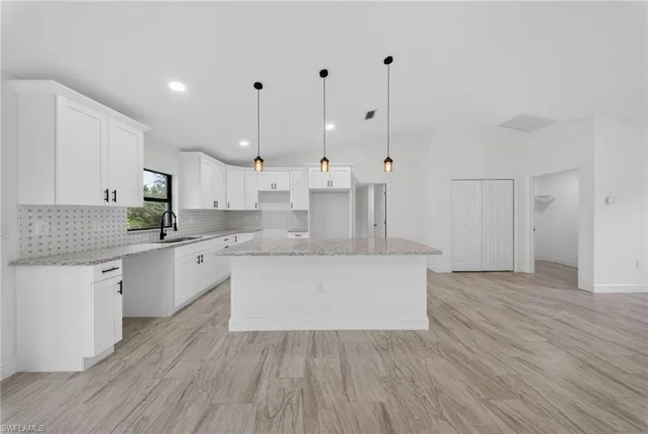 Kitchen featuring vaulted ceiling, white cabinets, light stone counters, backsplash, and a center island