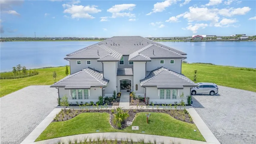 French provincial home with a water view, a tile roof, stucco siding, and a front lawn