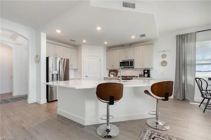 Kitchen with stainless steel appliances, arched walkways, light countertops, light wood-style floors, and an island with sink